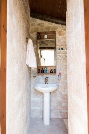 A bathroom with a stone wall, a white sink, and a wooden shelf above the mirror. - Myli Unique-Exotic Villa (Rethymno)