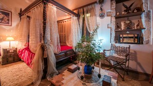 Ein traditionelles Himmelbett mit durchscheinenden Vorhängen, eine Holzbank, ein kleiner Tisch mit Kerzen und ein Regal mit Dekoration.