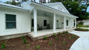 Una casa bianca a due piani con portico coperto, fondamenta in mattoni e un giardino anteriore curato con piccole piante e fiori.