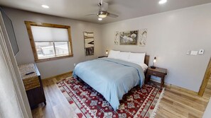 Quarto com cama, mesa de cabeceira e janela com persianas.