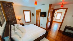 Ein Schlafzimmer mit einem großen Bett, Holzboden, einer Backsteinwand, einem Fernseher und einem Kamin.