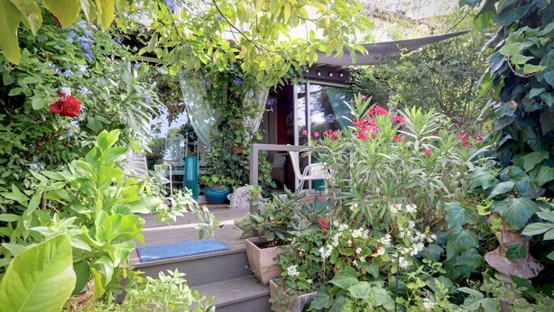 Un jardí amb escales que condueixen a una zona coberta, envoltat de plantes i flors diverses.