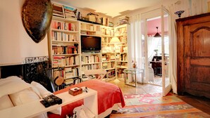 Un dormitori amb una gran biblioteca, una televisió i un llit amb llençol vermell.