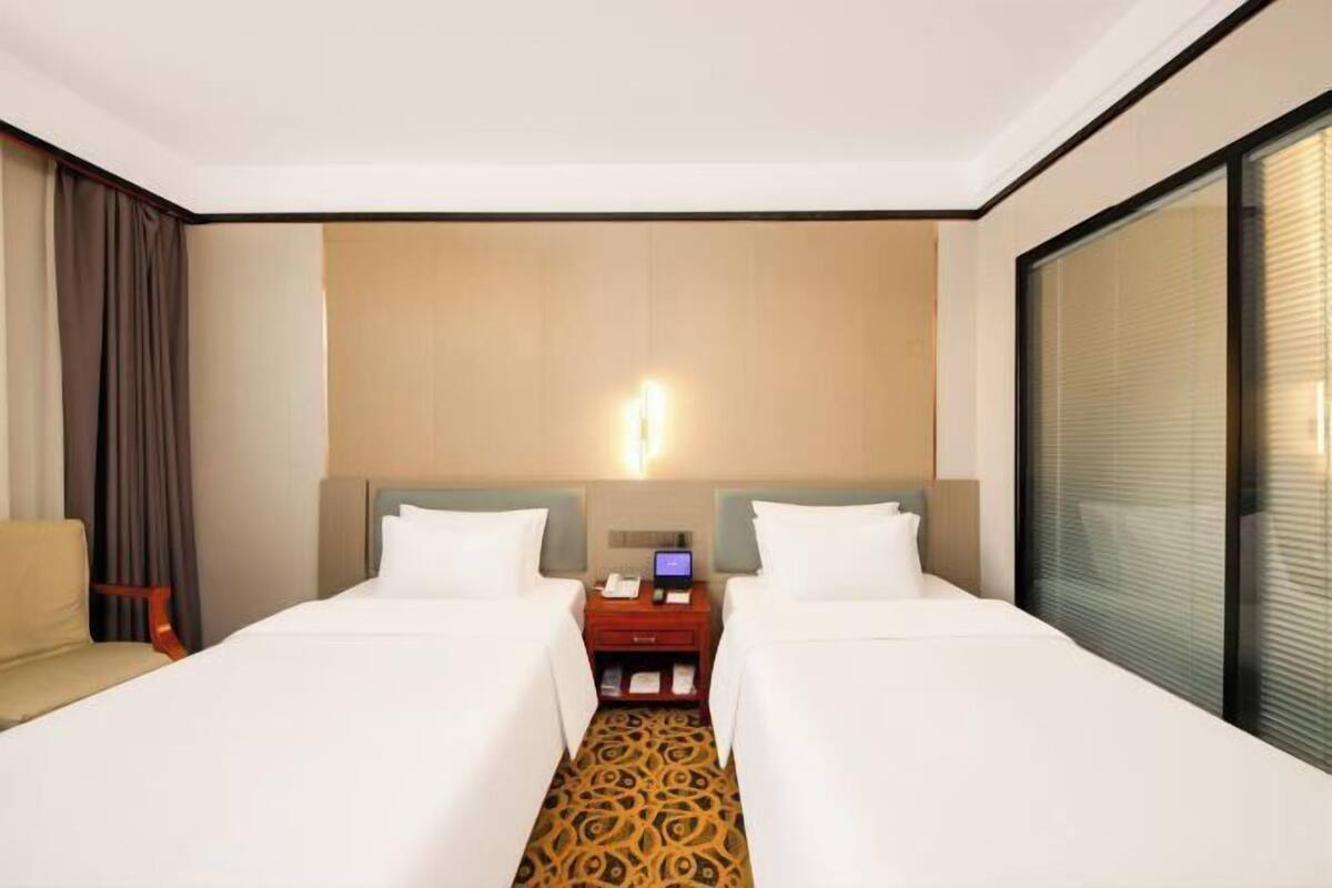 Une chambre d’hôtel avec deux lits, un bureau avec un ordinateur et une grande fenêtre.