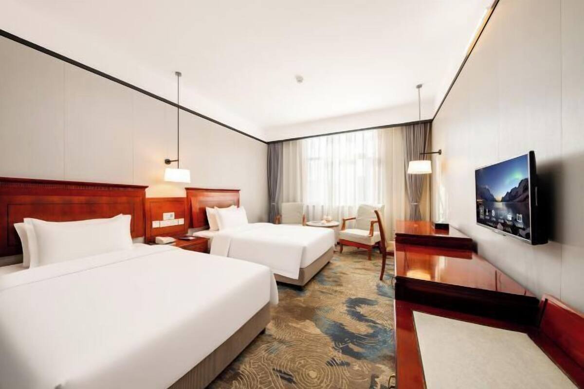 Une chambre d’hôtel avec deux lits, une télévision, un bureau, une chaise et une grande fenêtre avec des rideaux.