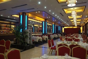 A banquet hall with round tables, red chairs, and a central plant. - Weilai Holiday Inn (Wuzhi)