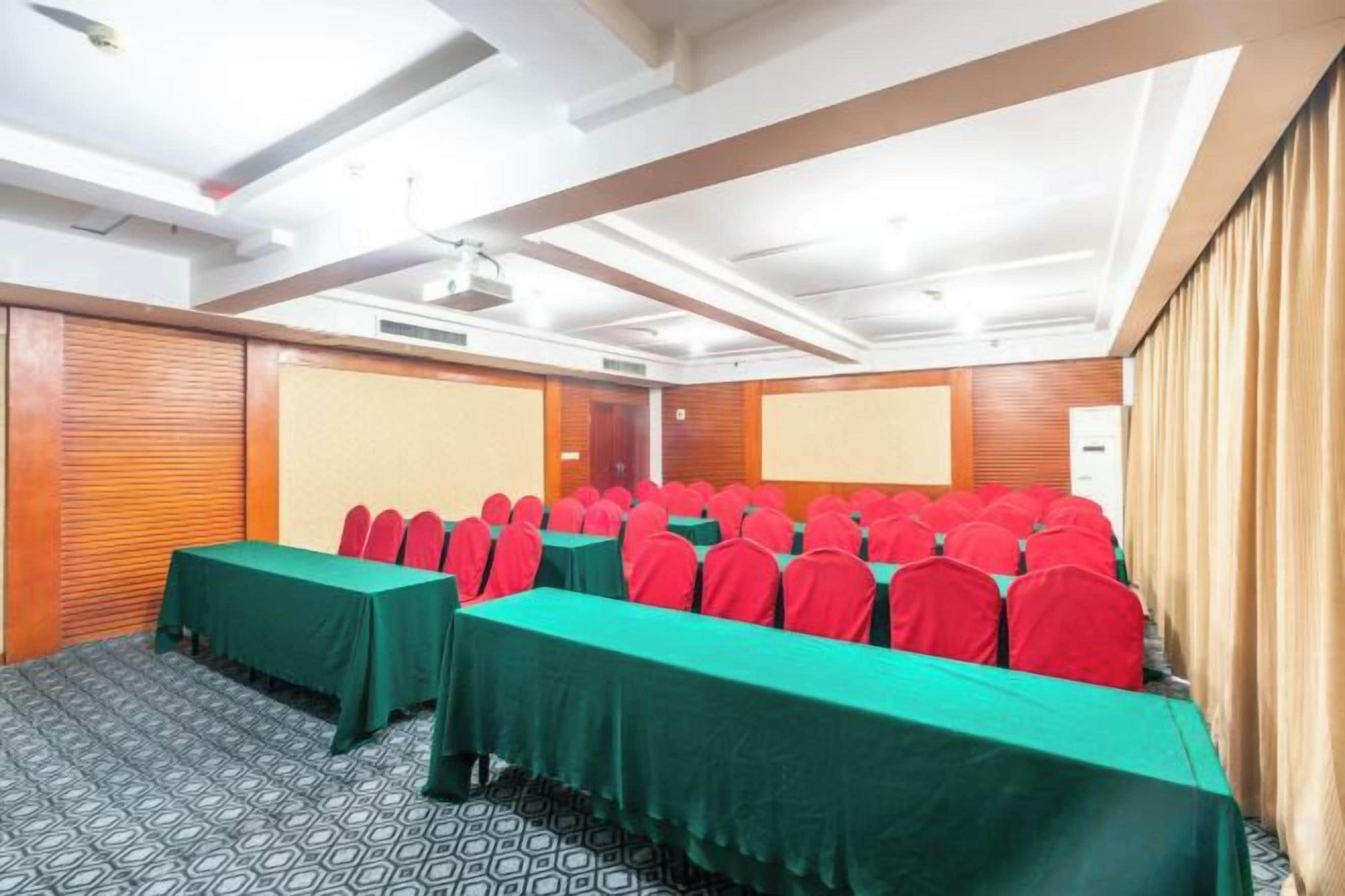A conference room with rows of tables and chairs, a projector screen, and a wooden panel wall.