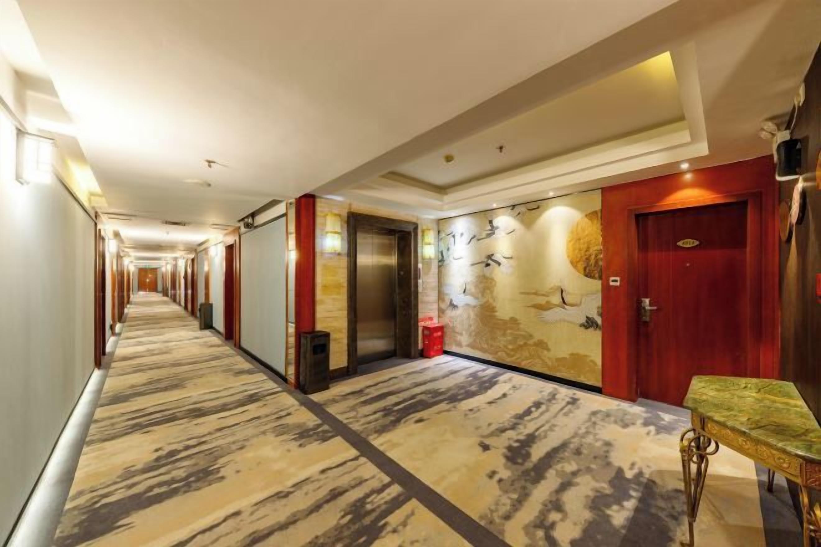 A hotel corridor with a carpeted floor, a red door, and a wall with a mural.