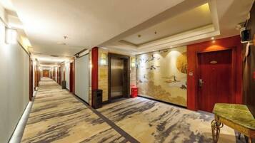 A hotel corridor with a carpeted floor, a red door, and a wall with a mural.