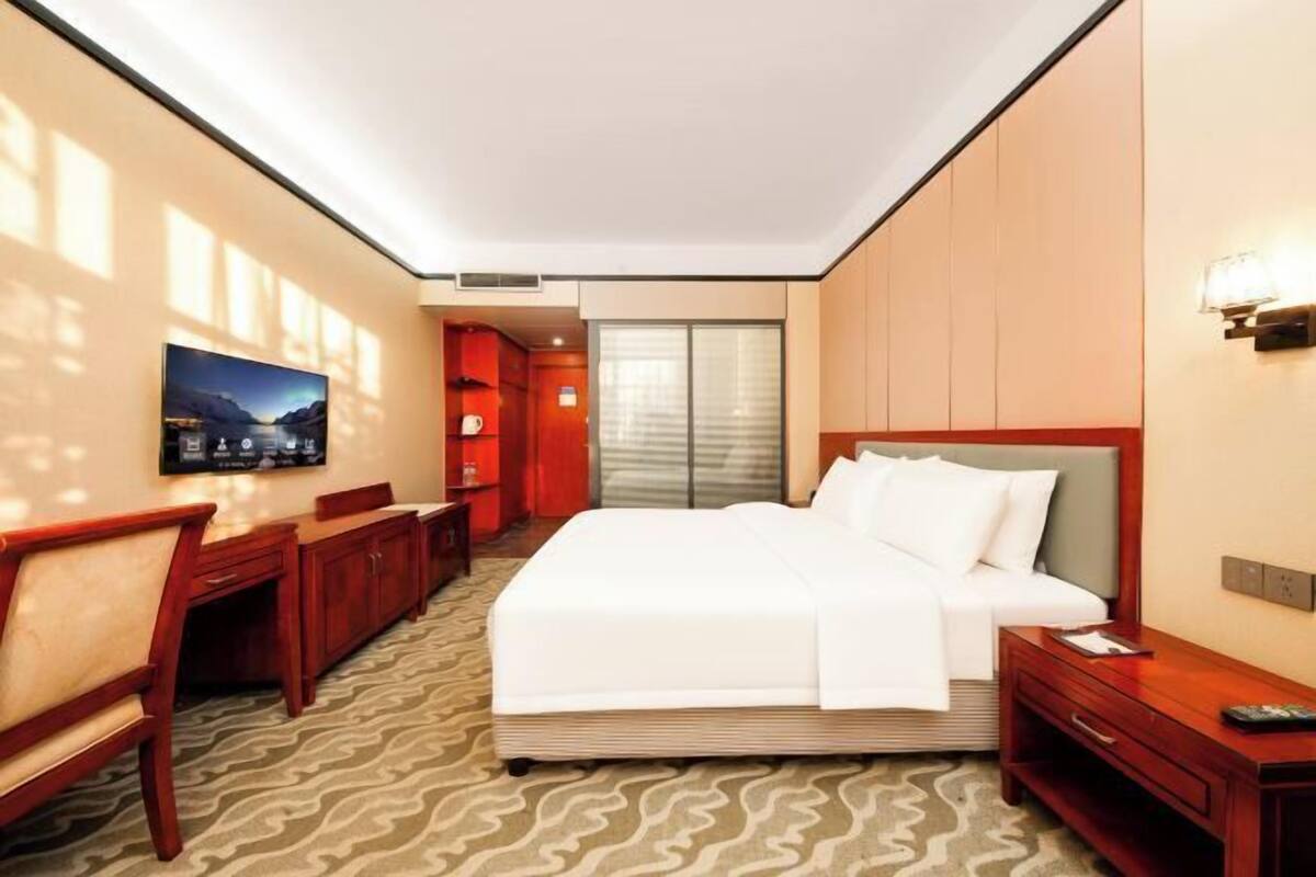 Une chambre d’hôtel avec un lit, un bureau, une chaise, une télévision et une fenêtre.