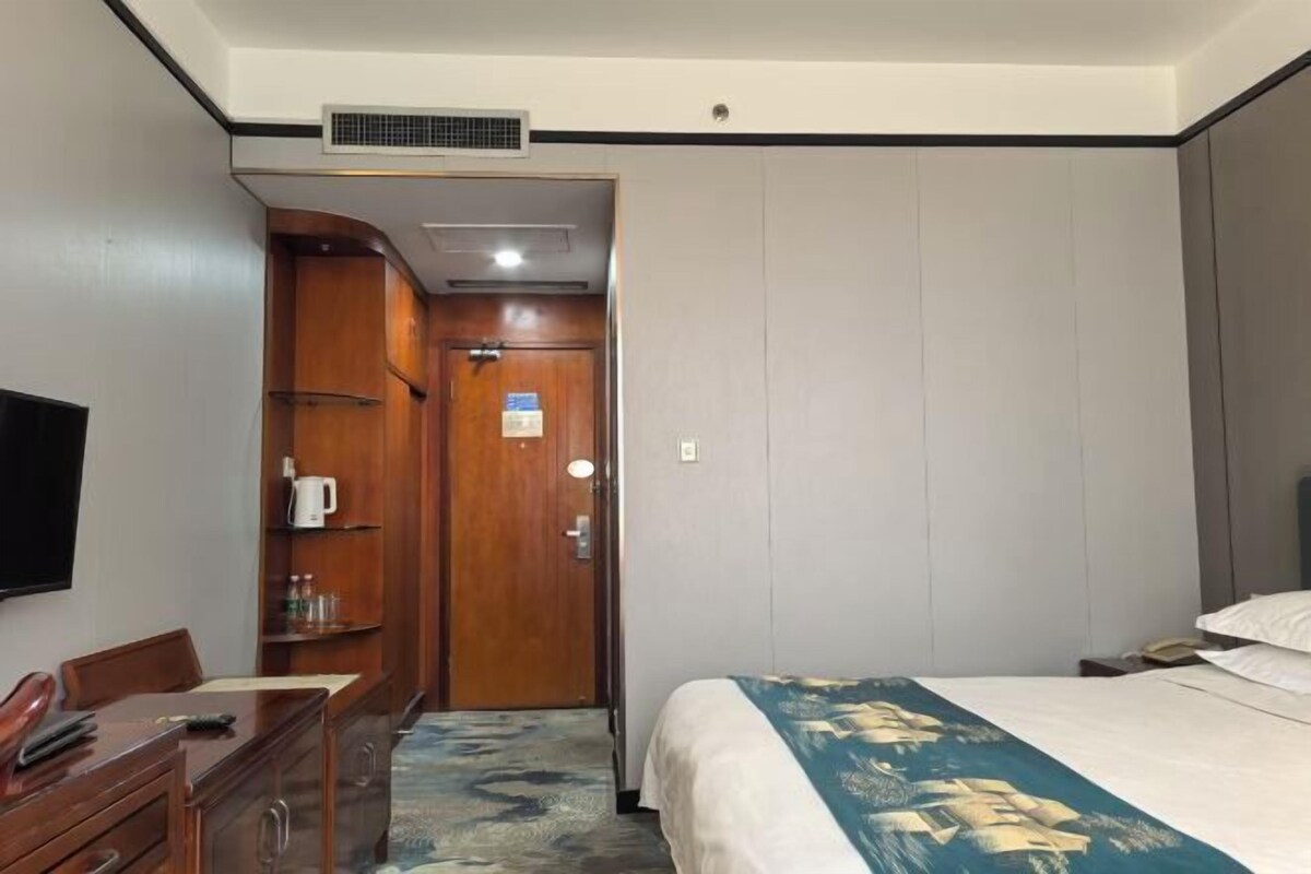 A hotel room with a bed, a desk with a chair, a wardrobe, and a television.