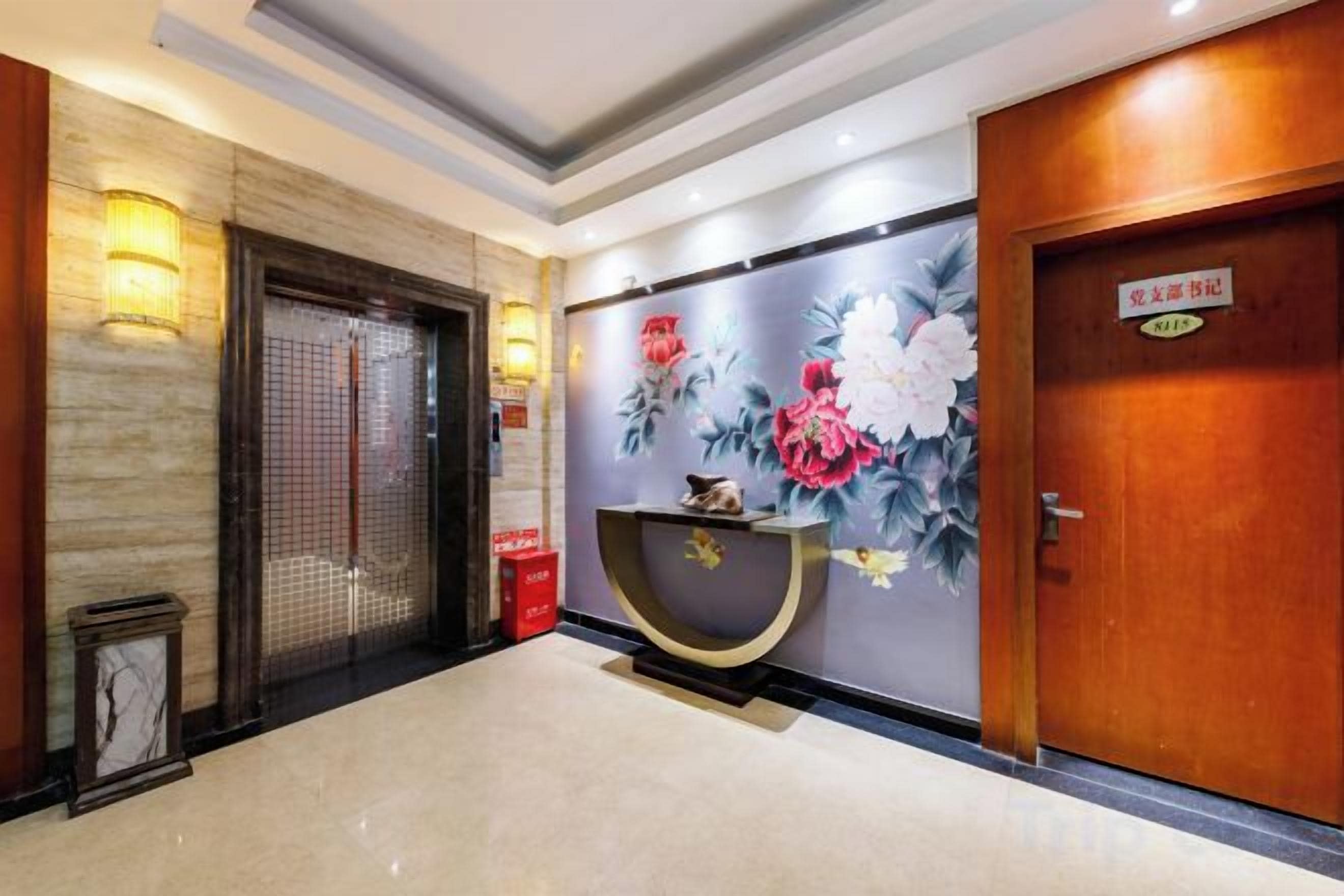 A hotel lobby with a reception desk, a wooden door, and a wall with floral artwork.