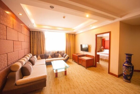 A hotel room with a sofa set, a glass coffee table, a TV, a bedside table, and a large mirror. - Weilai Holiday Inn (Wuzhi)