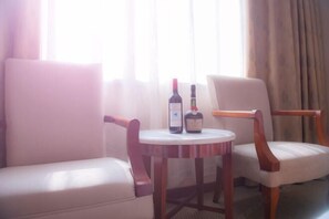 A room with two white leather chairs, a small round table with two bottles of wine, and a window with curtains. - Weilai Holiday Inn (Wuzhi)