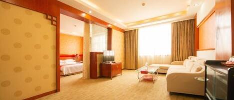 Habitación de hotel con cama, sofá, televisor, escritorio y ventana con cortinas.