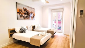 A hotel room with two beds, a large painting on the wall, and a window with a view of buildings.