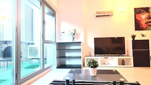 A modern living room with a large TV, a glass door leading to a balcony, and a minimalist design.
