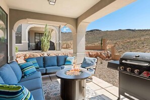An outdoor patio with a fire pit, a barbecue grill, and blue cushioned seating.