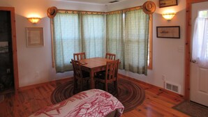 A dining area with a wooden table and chairs, a patterned rug, and a bay window with curtains.