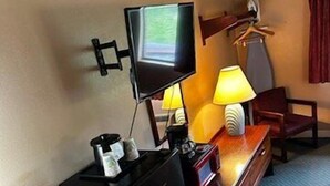 A hotel room with a desk, a television mounted on the wall, a lamp, a chair, and a bed. - Home Place Inn (Nicholasville)