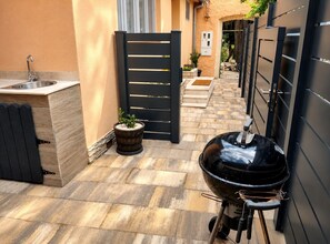 Une petite terrasse extérieure avec un barbecue, un évier et un portail.