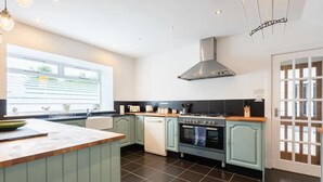 A modern kitchen with a large island, a gas stove, a built-in oven, and a window providing natural light. - 5 Bedrooms, Sleeps 10-12 w/ Wifi, Parking & Garden (Leven)