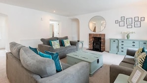 A living room with a grey sofa set, a light blue ottoman, a fireplace, and a teal cabinet. - 5 Bedrooms, Sleeps 10-12 w/ Wifi, Parking & Garden (Leven)