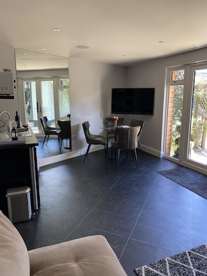 Un salon moderne comprenant un coin repas, un téléviseur à écran plat fixé au mur et une grande porte-fenêtre coulissante donnant sur un jardin.