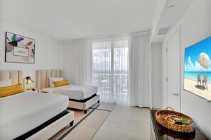 Une chambre d’hôtel avec deux lits, une grande fenêtre avec des rideaux légers, une œuvre d’art encadrée au mur et un tableau représentant une scène de plage.