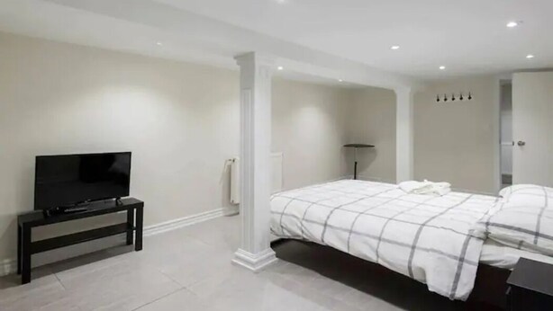 Un dormitorio con cama, televisor sobre un mueble bajo, mesita de noche y lámpara.