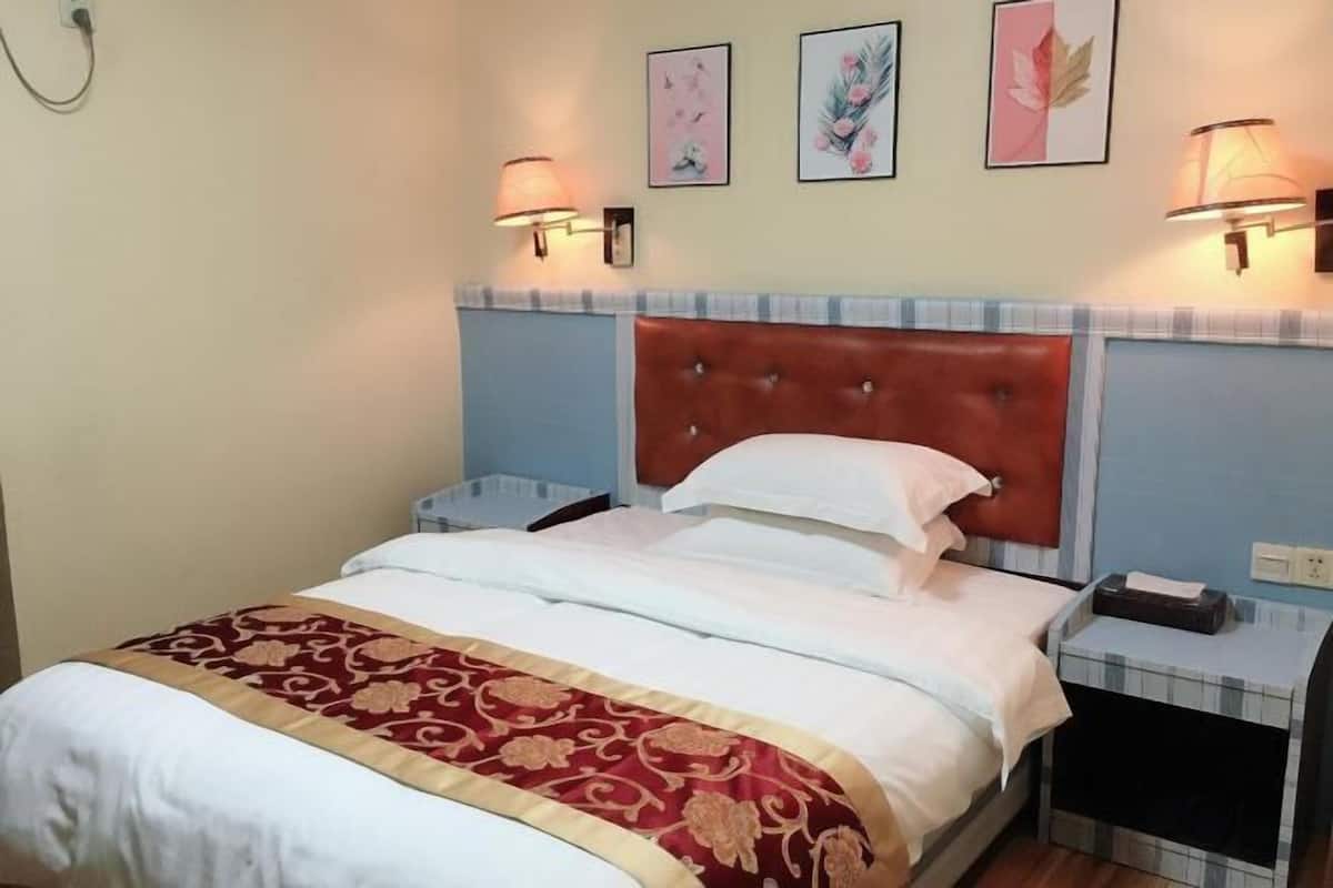 A neatly made bed with a red and gold bedspread, a tufted headboard, and two bedside tables with lamps.