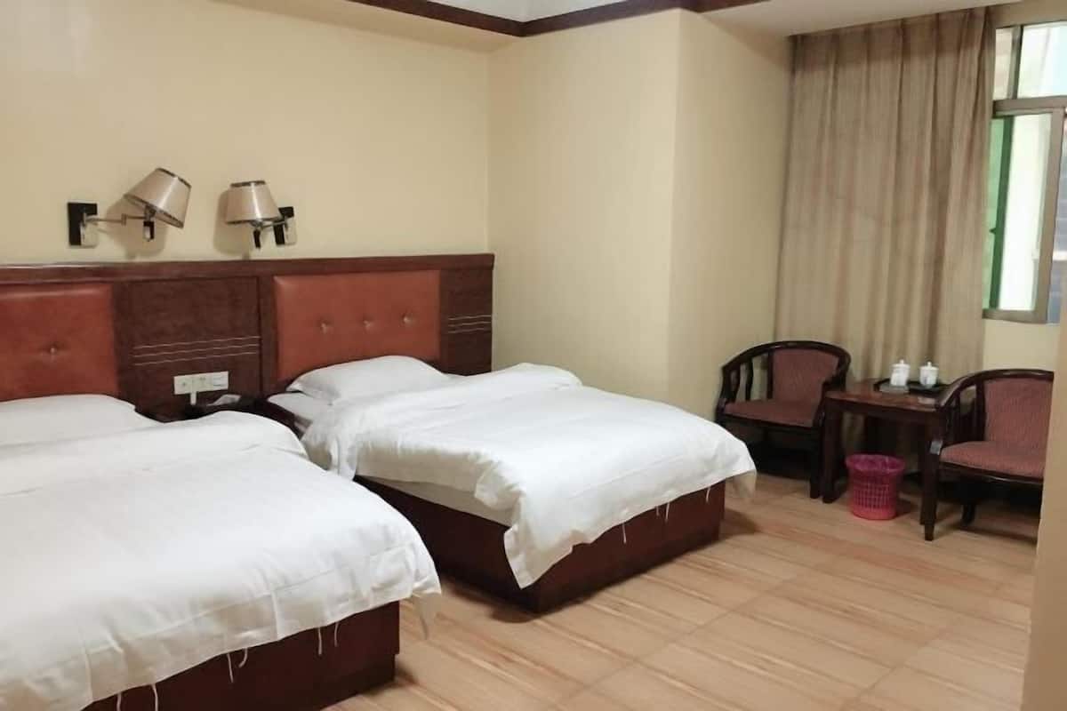 A hotel room with two beds, a wooden headboard, a small table with chairs, and a window with curtains.