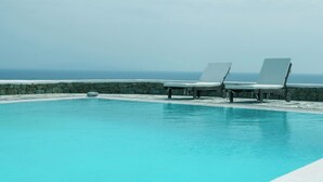 A pool with two lounge chairs and a stone wall. - Villa Super Three (Mykonos)