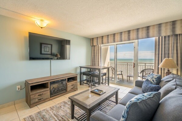 Una sala de estar con sofá, mesa de centro, televisor y un balcón con vistas al mar.