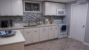 A modern kitchen with white cabinets, a microwave, a stove, and a sink. - Roanoke’s modern Lower Level Apt. (Basement). (Roanoke)