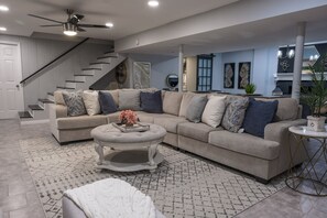 A spacious living room with a sectional sofa, a round coffee table, and a staircase leading to an upper level.