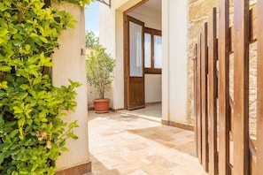 Stroll through the tranquil corridor, lined with lush foliage and a potted plant, to a traditional wooden door with glass panels.