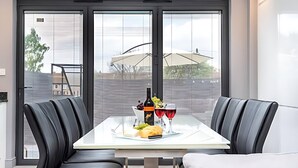 Een moderne eetruimte met een tafel gedekt voor twee personen, compleet met een fles wijn, een glas, een brood en een fruitmand.