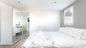 Een moderne slaapkamer met een groot bed, een glazen scheidingswand en een raam met jaloezieën.