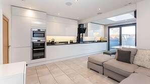 Een moderne keuken met inbouwapparatuur, een zithoek met een bank en een groot raam dat voor natuurlijk licht zorgt.