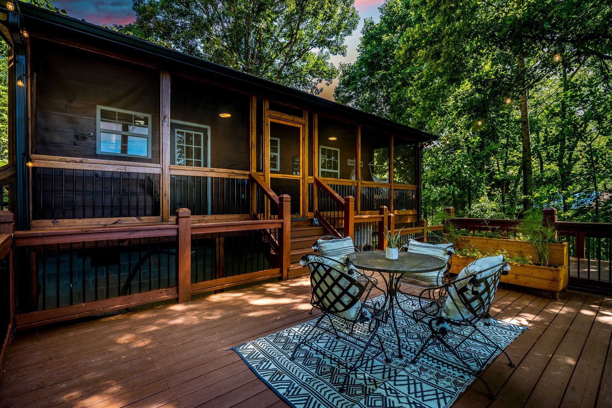 A wooden deck with a table and chairs, surrounded by lush greenery.