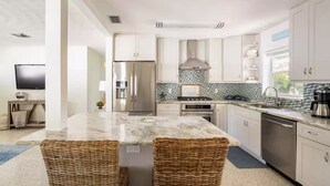 A modern kitchen with white cabinets, a marble island, stainless steel appliances, and a tiled backsplash.