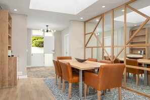 Un espace de salle à manger moderne avec une table en bois et des chaises orange, un tapis à motifs géométriques et une vue sur la verdure à l’extérieur.
