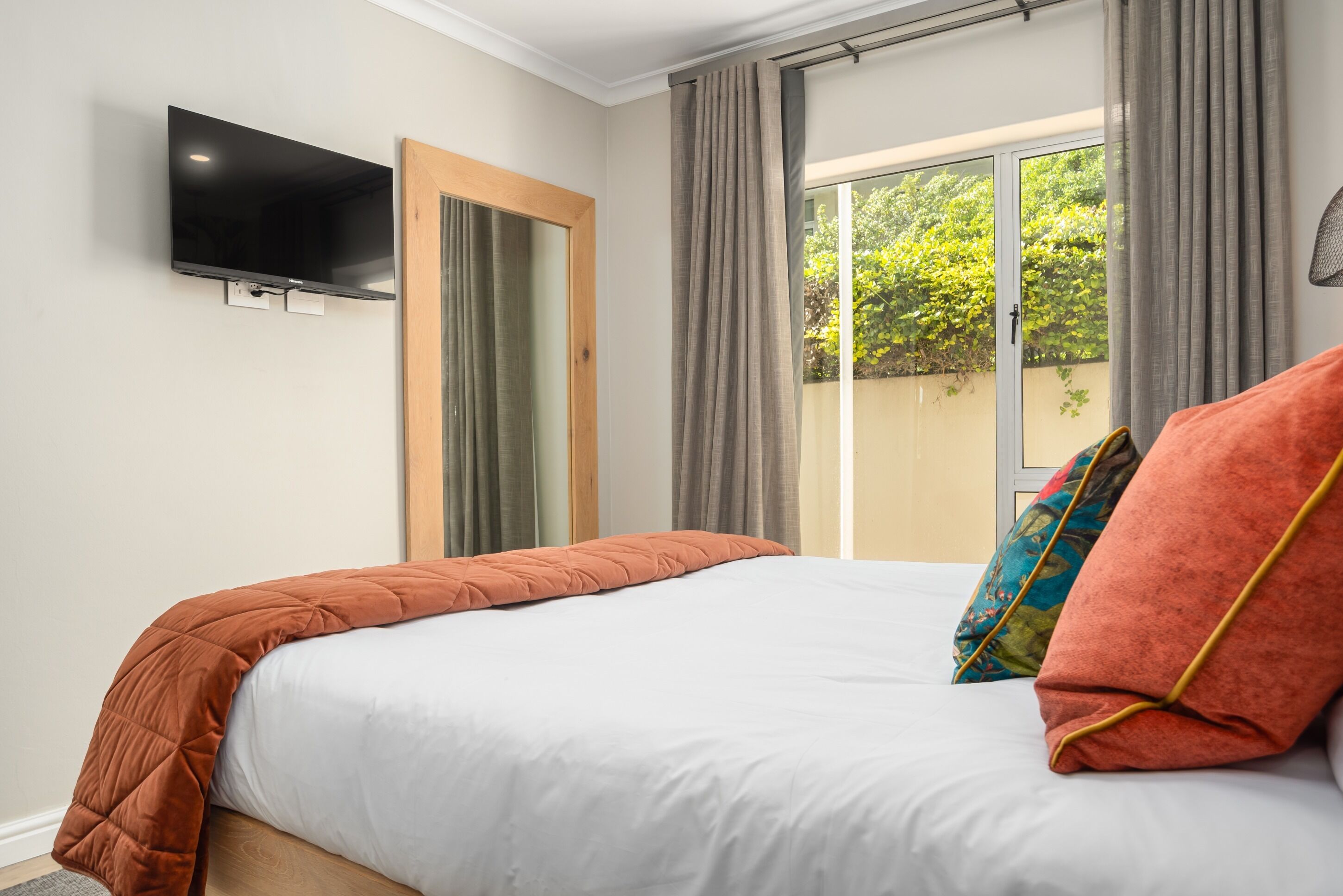 A bedroom with a bed, a TV mounted on the wall, and a window with curtains.