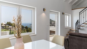 A modern living room with a white table, a vase with dried plants, and a view of the sea through large windows. - Seaview Villa KING with pool 3km from sea (Omis)