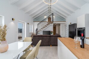 A modern kitchen with a wooden island, a dining area with chairs, a staircase, and a view of the outdoors.