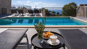A poolside area with lounge chairs, a table with a croissant and a cup, and a view of the sea. - Seaview Villa KING with pool 3km from sea (Omis)
