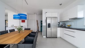 Una cocina moderna con armarios blancos, un refrigerador de acero inoxidable y una mesa de comedor de madera con sillas negras.