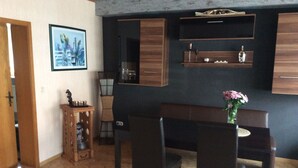 A dining area with a wooden table and chairs, a small cabinet with decorative items, and a framed picture on the wall.