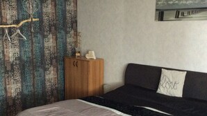A bedroom with a bed, a wardrobe, a hanging light fixture, and a wall tapestry.